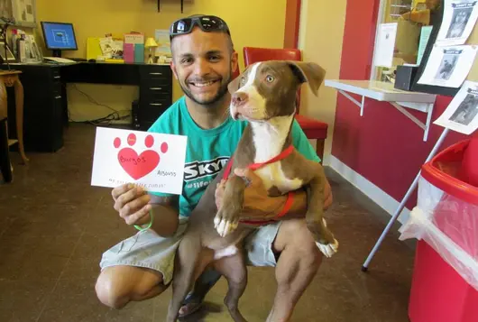 Man crouched down with one arm around dog and the other holding up a sign with a heart on it