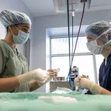 Two medical clinicians perform surgery wearing masks, nets, and scrubs 