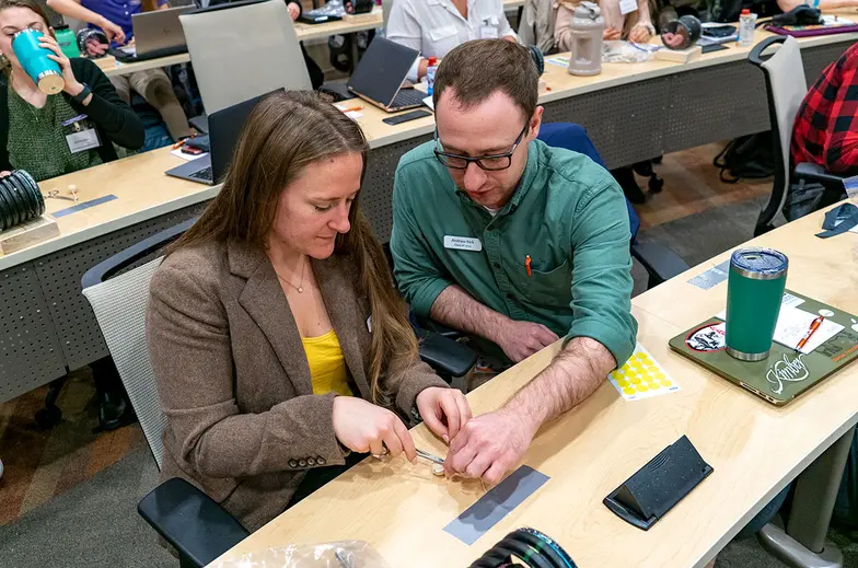 Veterinary students sit at a desk in a large lecture oom learning various animal techniques