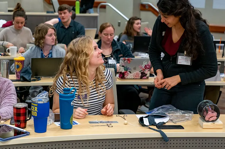 Veterinary students sit at a desk in a large room learning various animal techniques