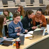 Veterinary students sit at a desk in a large room learning various animal techniques