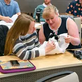 Veterinary students sit at a desk in a large room learning various animal techniques