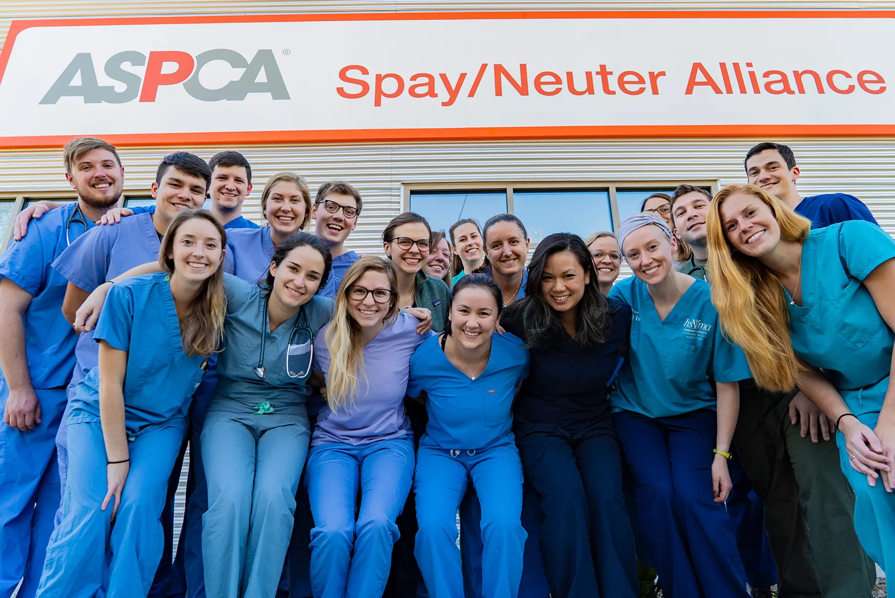 group of students wearing scrubs standing outside ASNA building in front of signage